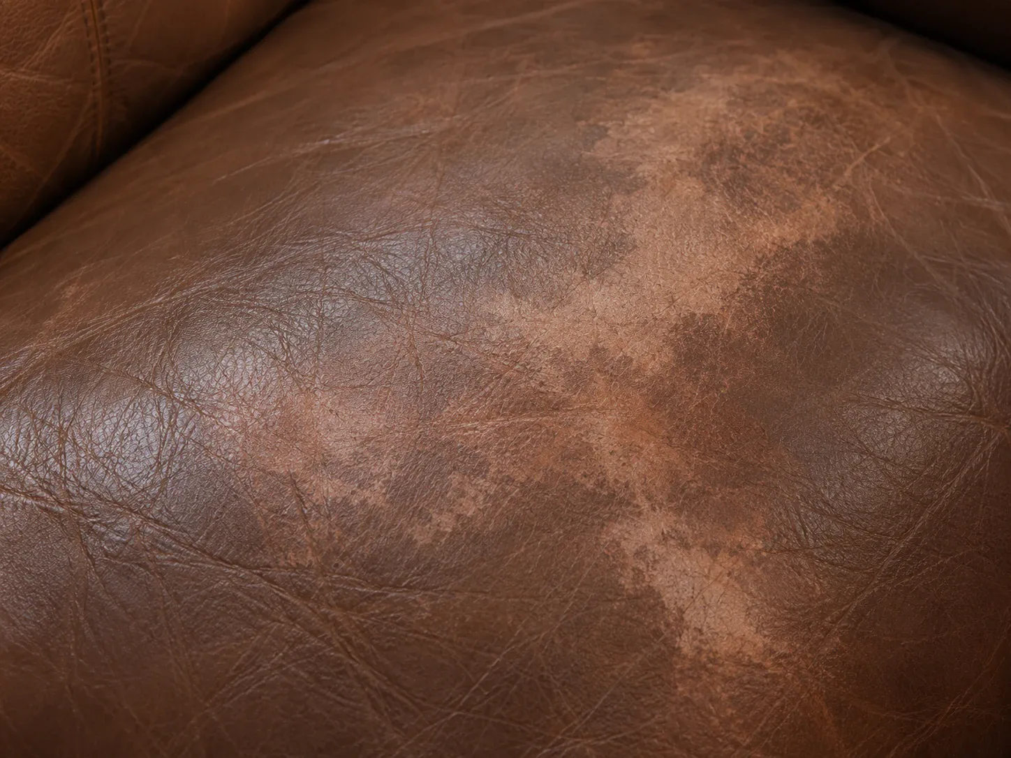 Blotchy patch of lighter tone across an otherwise even brown leather cushion