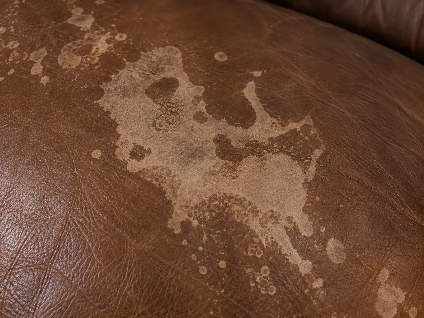 Pale rings and tidelines dried into the surface of a brown leather cushion