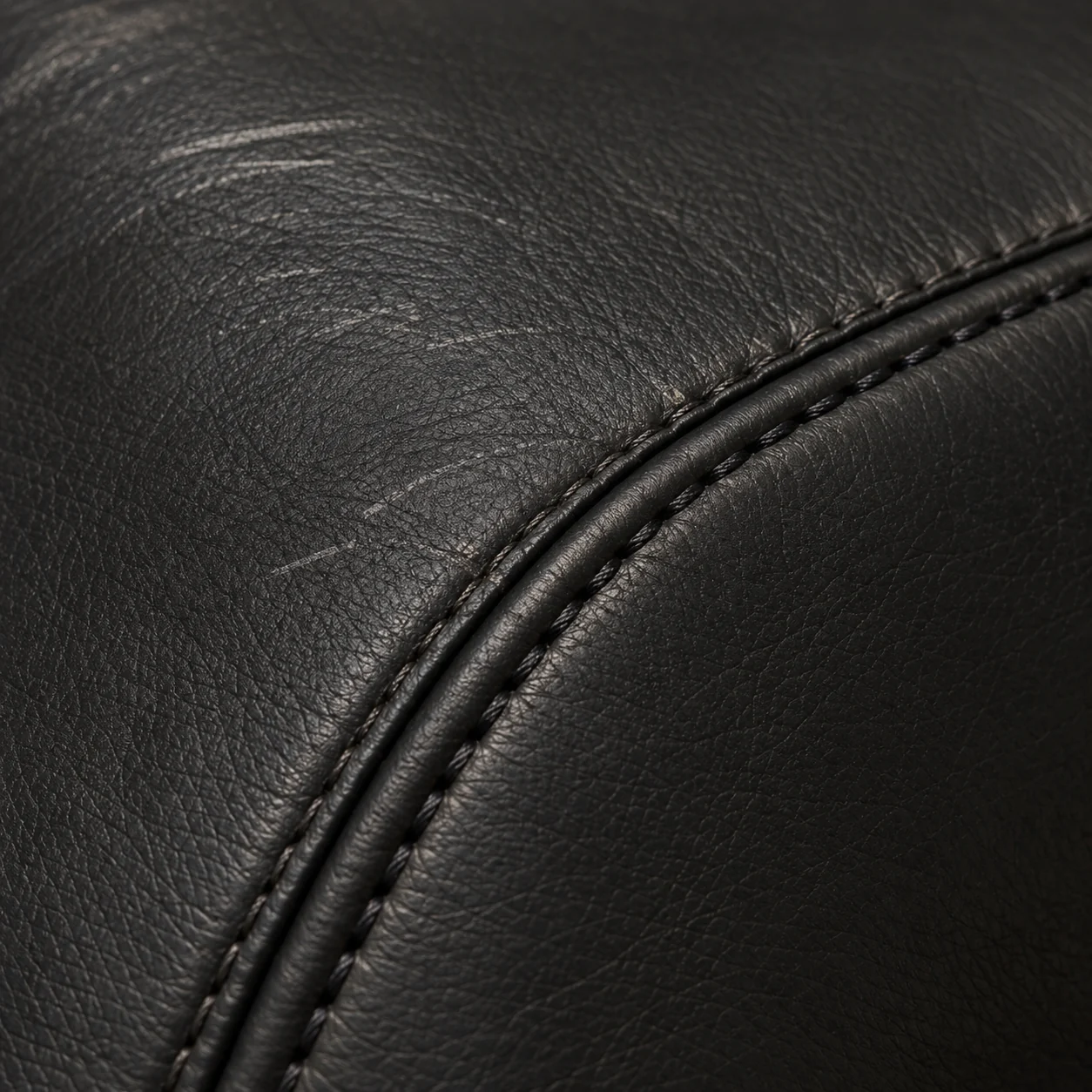 Faint surface scratches on dark grey leather beside a stitched seam