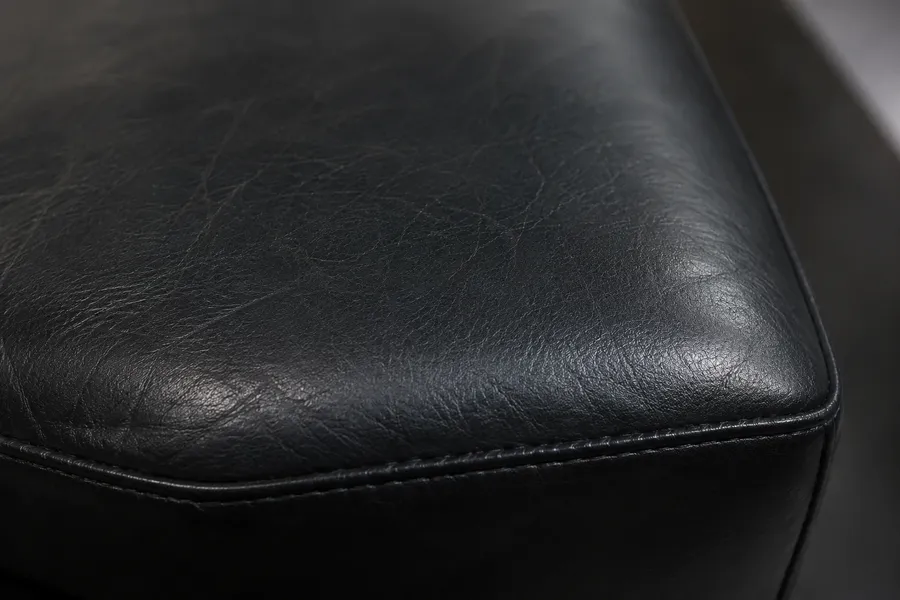 Corner of a black aniline leather cushion with a fine scratch showing darker than the surrounding hide