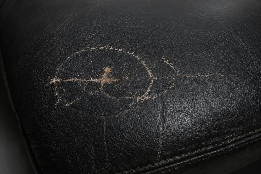 Black pigmented leather scored with a ring of scratches that cut through the colour coating to a paler layer beneath