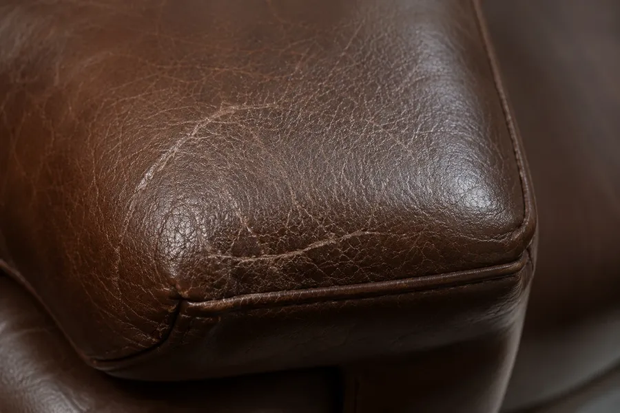 Corner of a brown semi-aniline leather cushion with a long scratch running across the front face