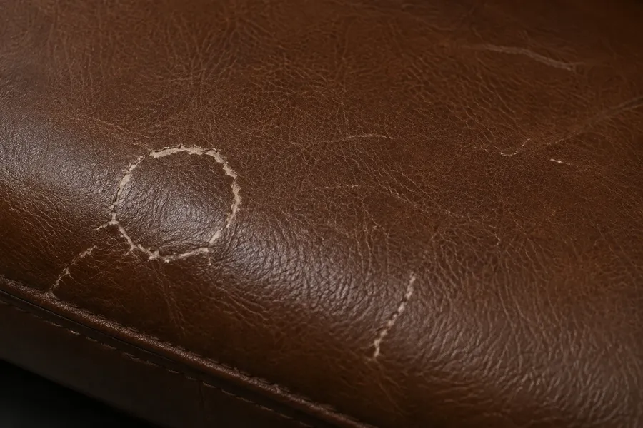 Dark brown top-grain leather with scratches cutting through the embossed grain and exposing a lighter layer