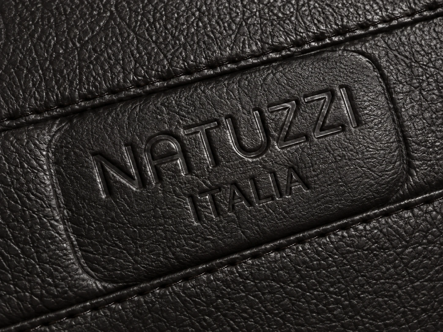 The NATUZZI ITALIA nameplate embossed into black pebbled leather beside a stitched seam
