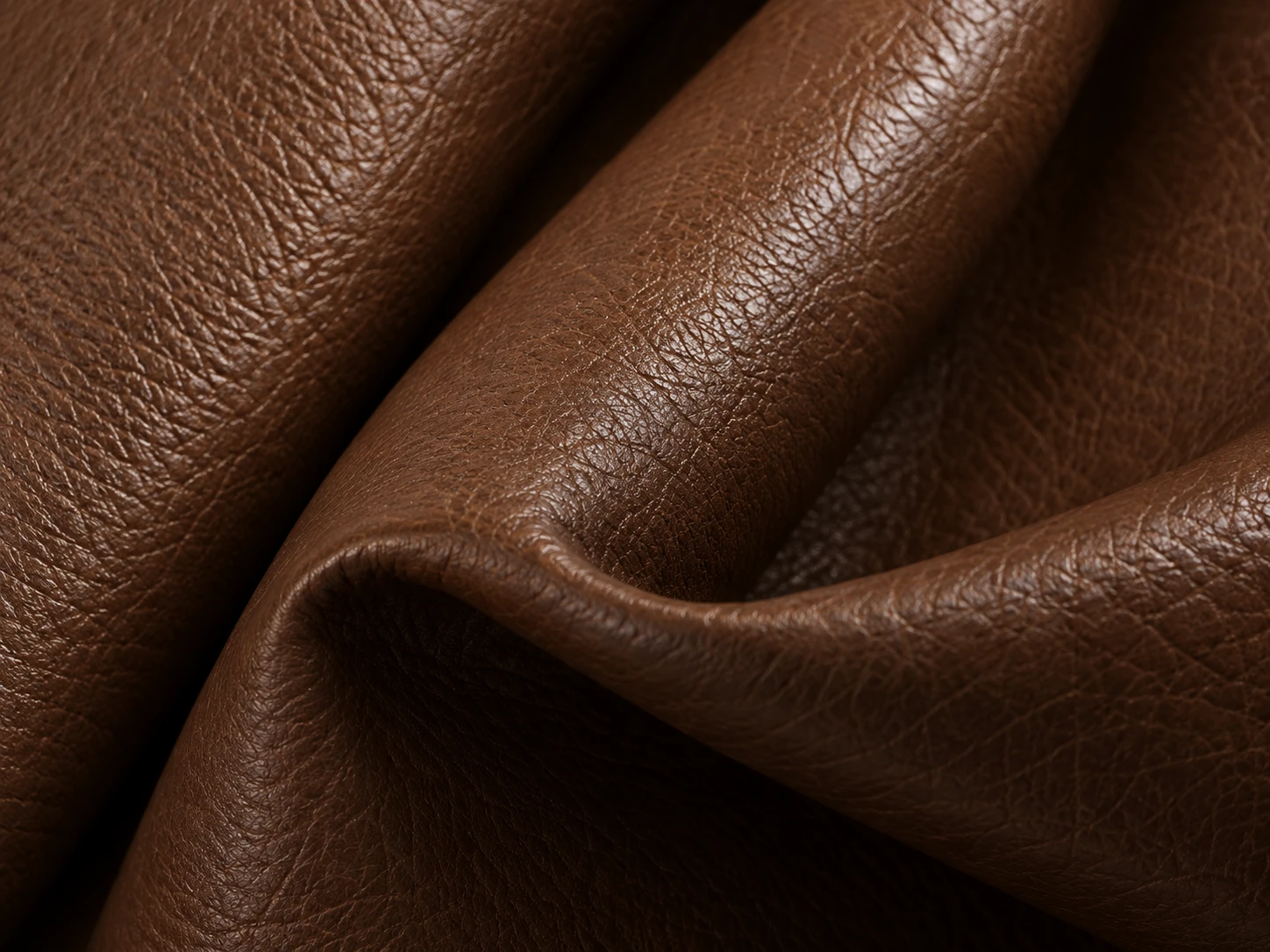 A soft fold in cognac leather showing the open grain and natural sheen of the hide