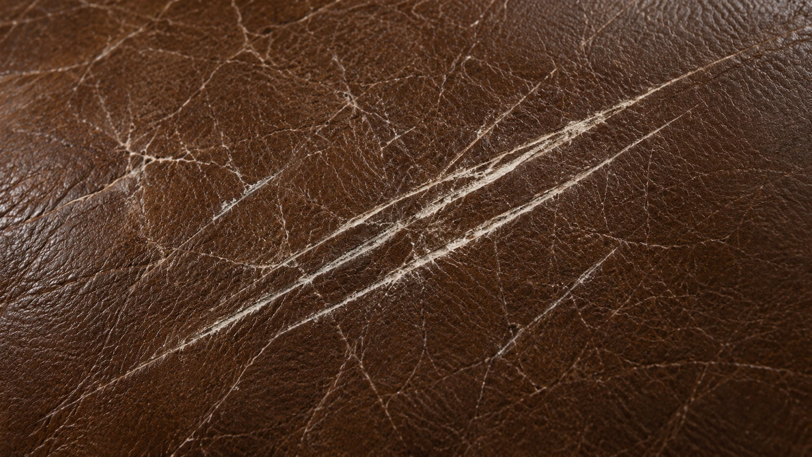 Two pale scratch lines cut across the grain of a brown Natuzzi leather seat