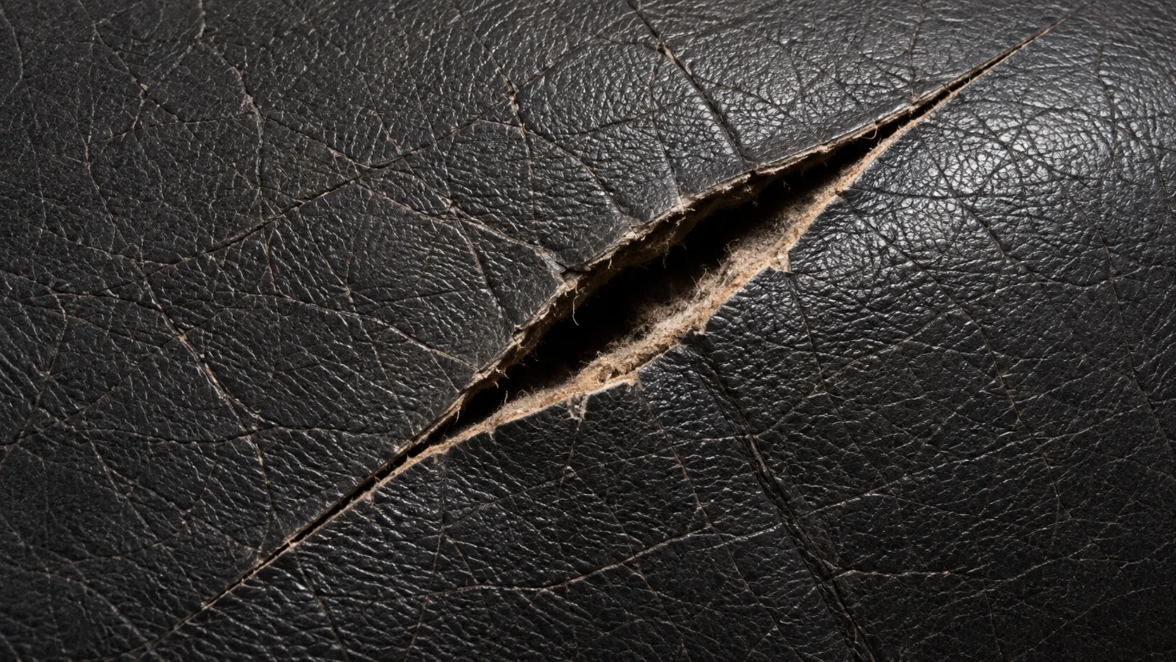 An open split in black leather with the pale fibre backing showing through