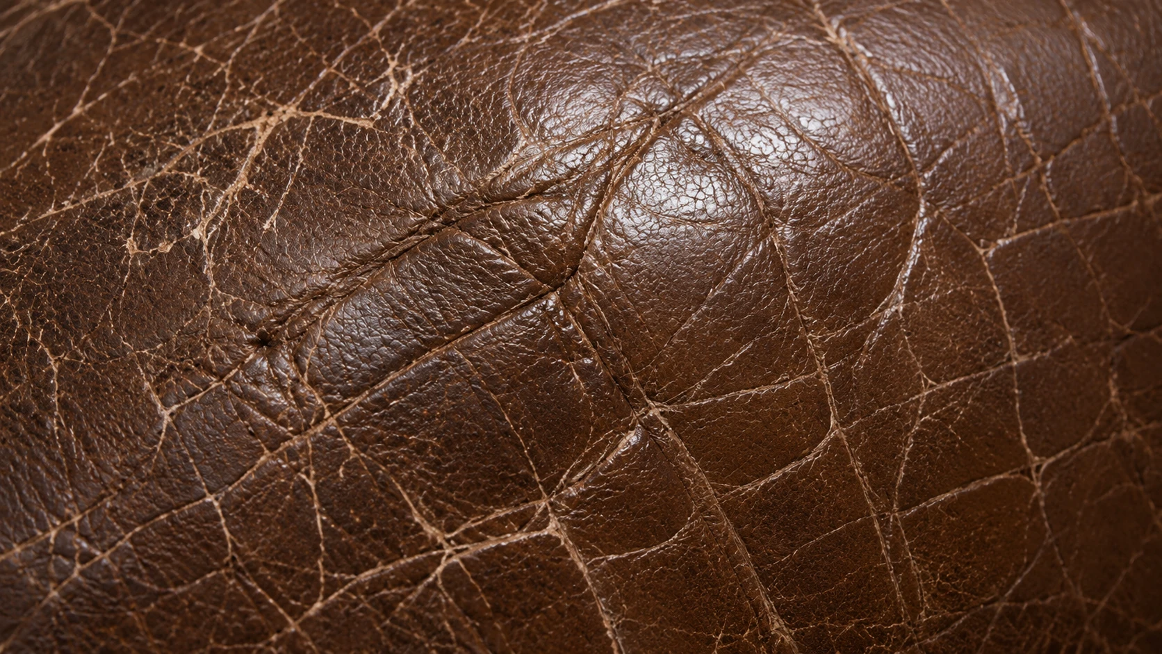 Surface crazing and a set crease along a worn brown leather seat