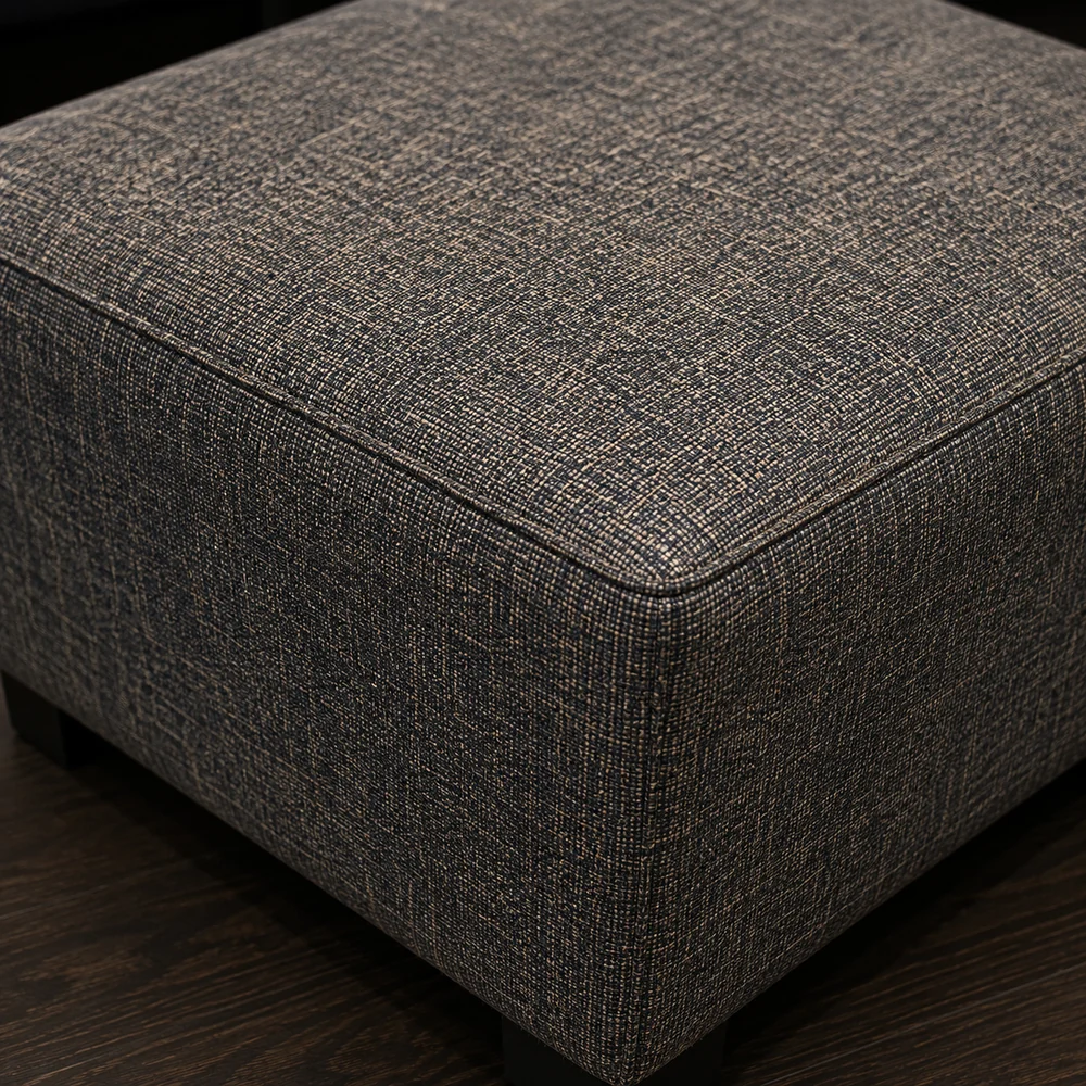 Corner of a grey woven fabric ottoman showing the texture of the weave