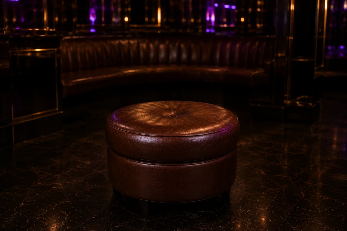 Round leather ottoman on a polished club floor with banquette seating behind