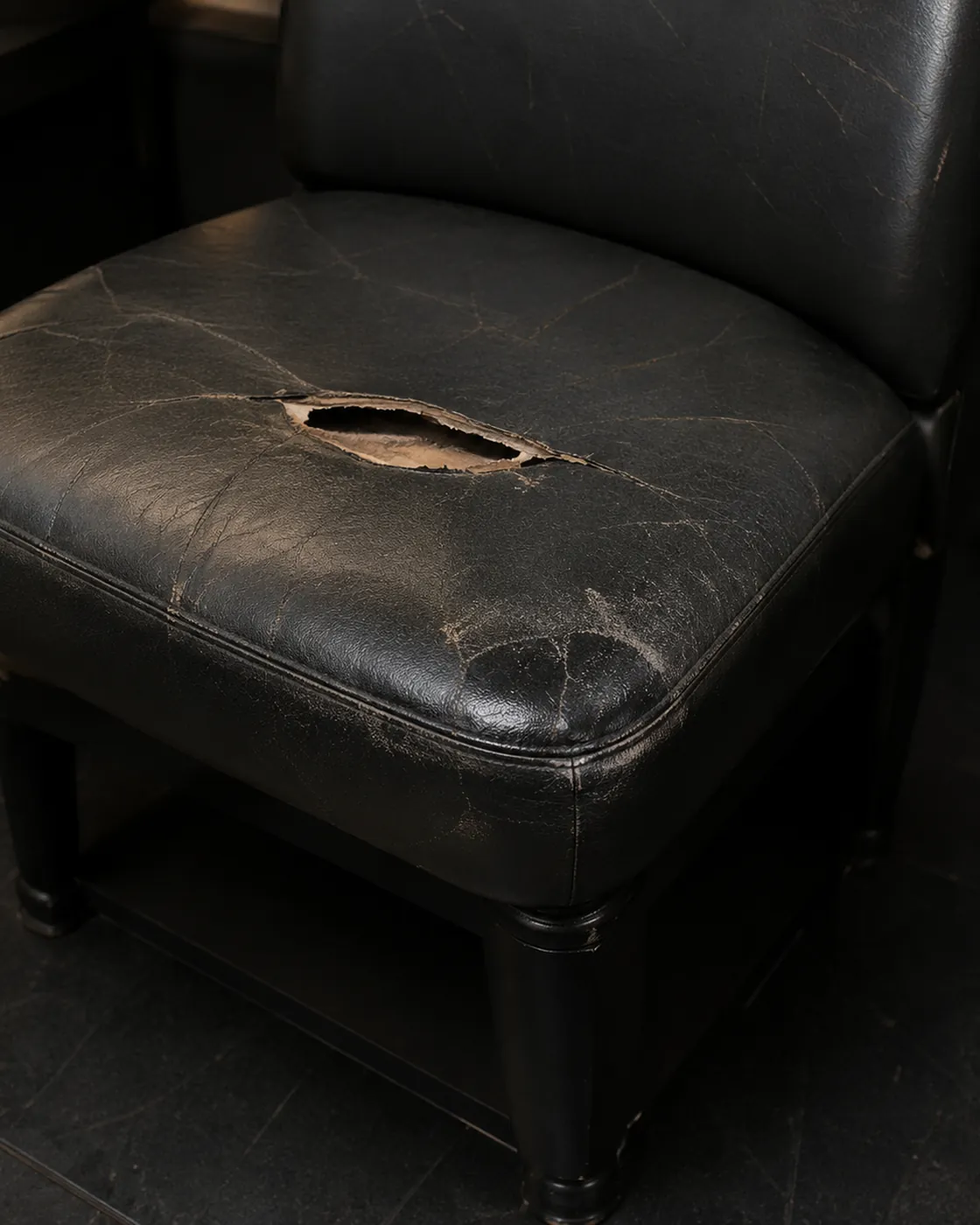 A black nightclub club chair with the leather seat split open