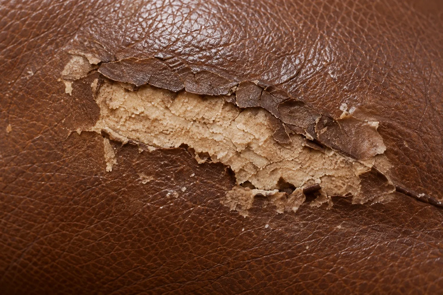 Pale filler from an earlier repair breaking up under brown leather