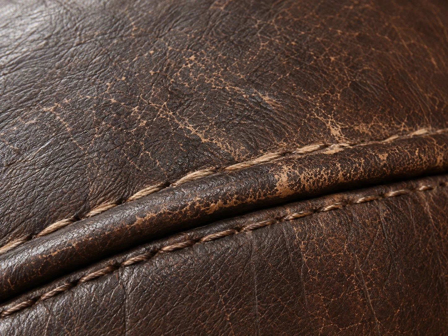 Worn brown leather panel with crazing along the piped edge