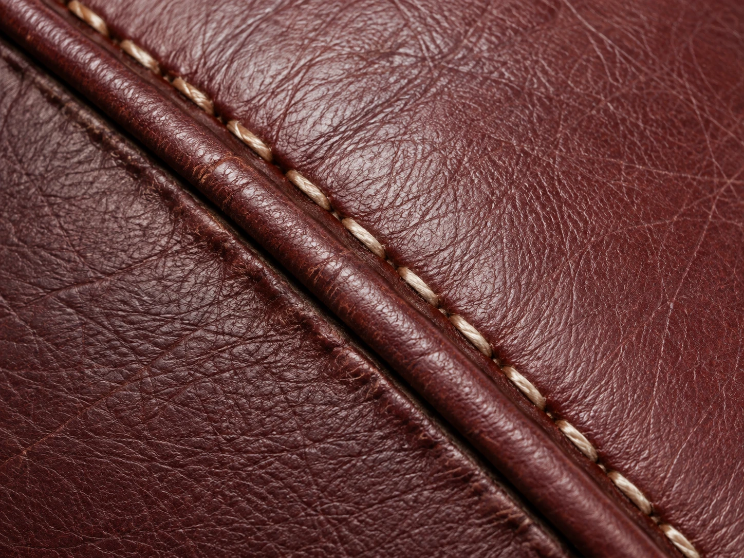 Close inspection of stitching along oxblood leather piping