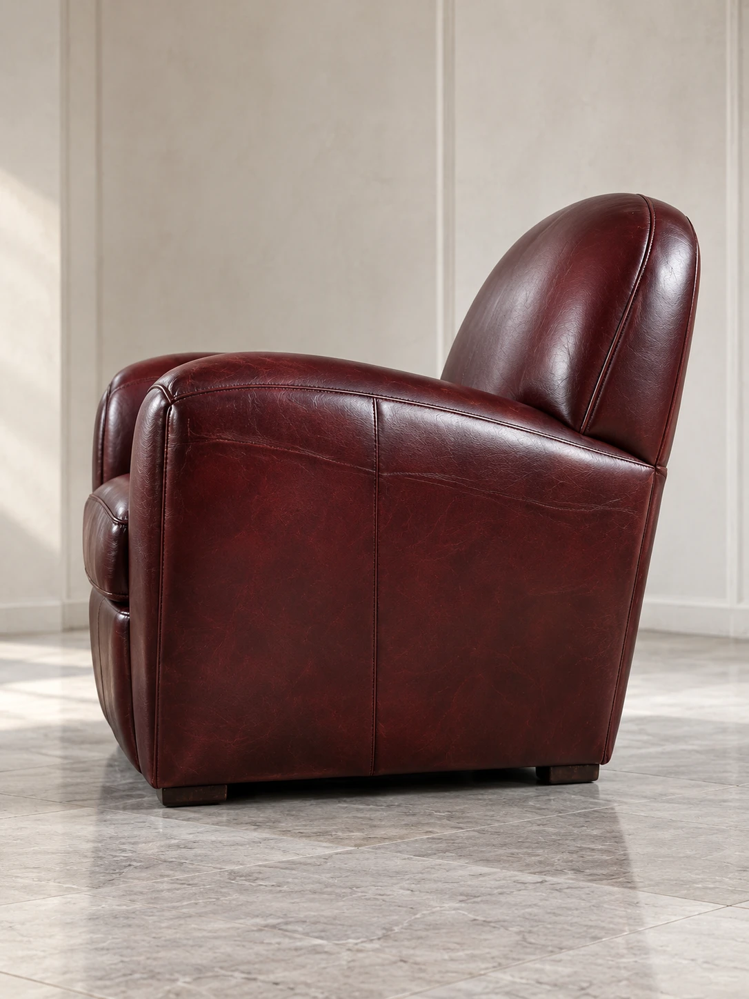 Side profile of an oxblood leather club chair on a marble floor