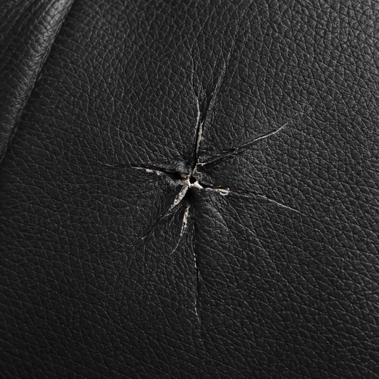A star-shaped puncture through the black leather back panel of a massage chair