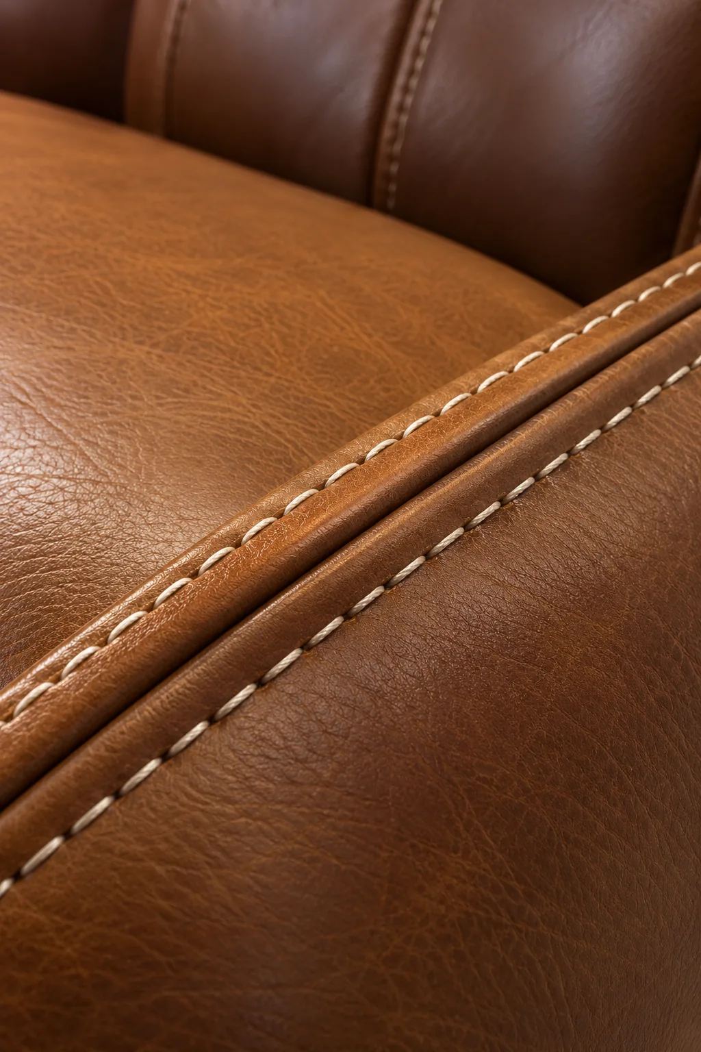 A close view of tan leather where two parallel rows of cream contrast stitching run either side of a welted seam