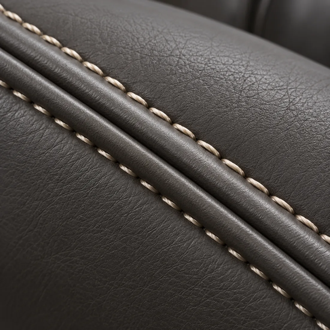 A close view of dark grey leather finished with two parallel covered cords and cream contrast stitching