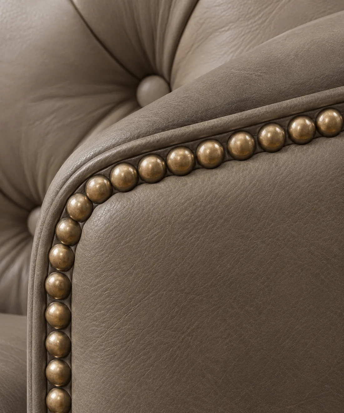 A close view of a taupe buttoned leather chair with a line of domed brass nailheads set along the arm