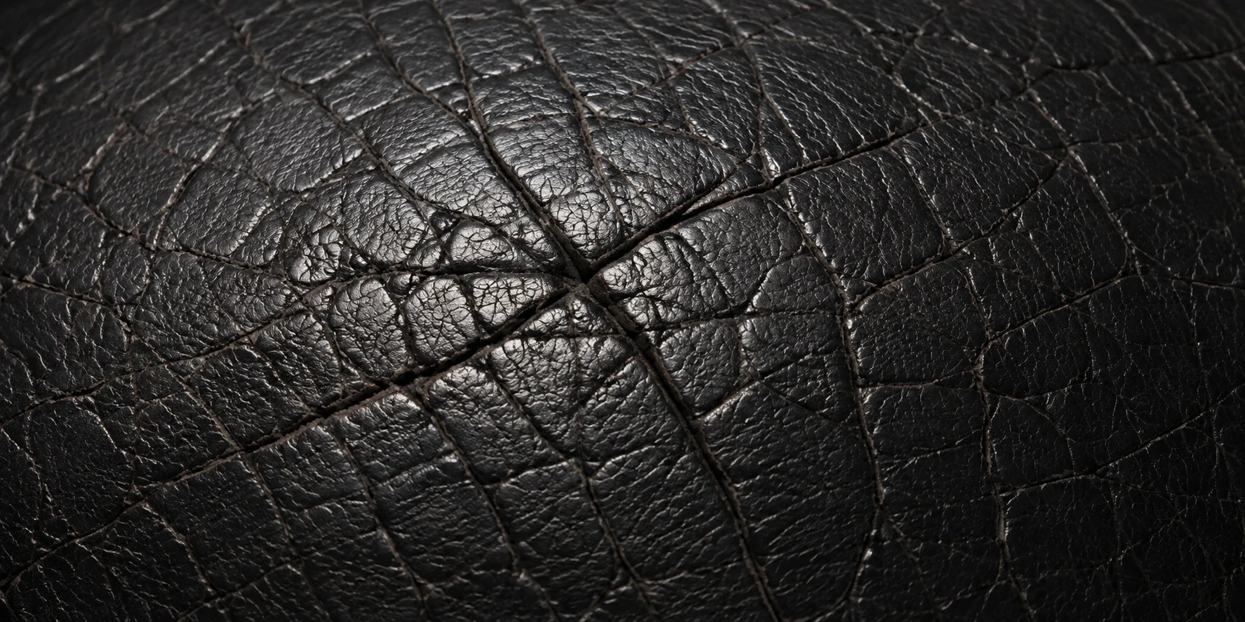 Deep crack network spreading across a black leather seat panel
