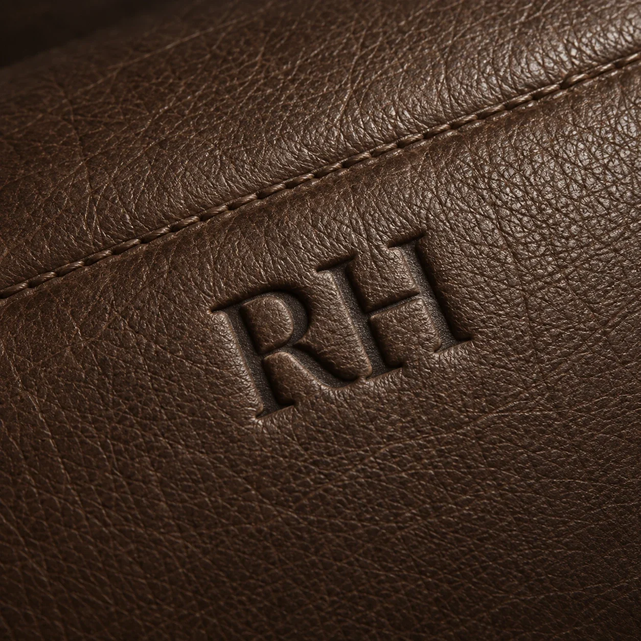 An embossed RH monogram pressed into a brown leather panel beside a stitched seam