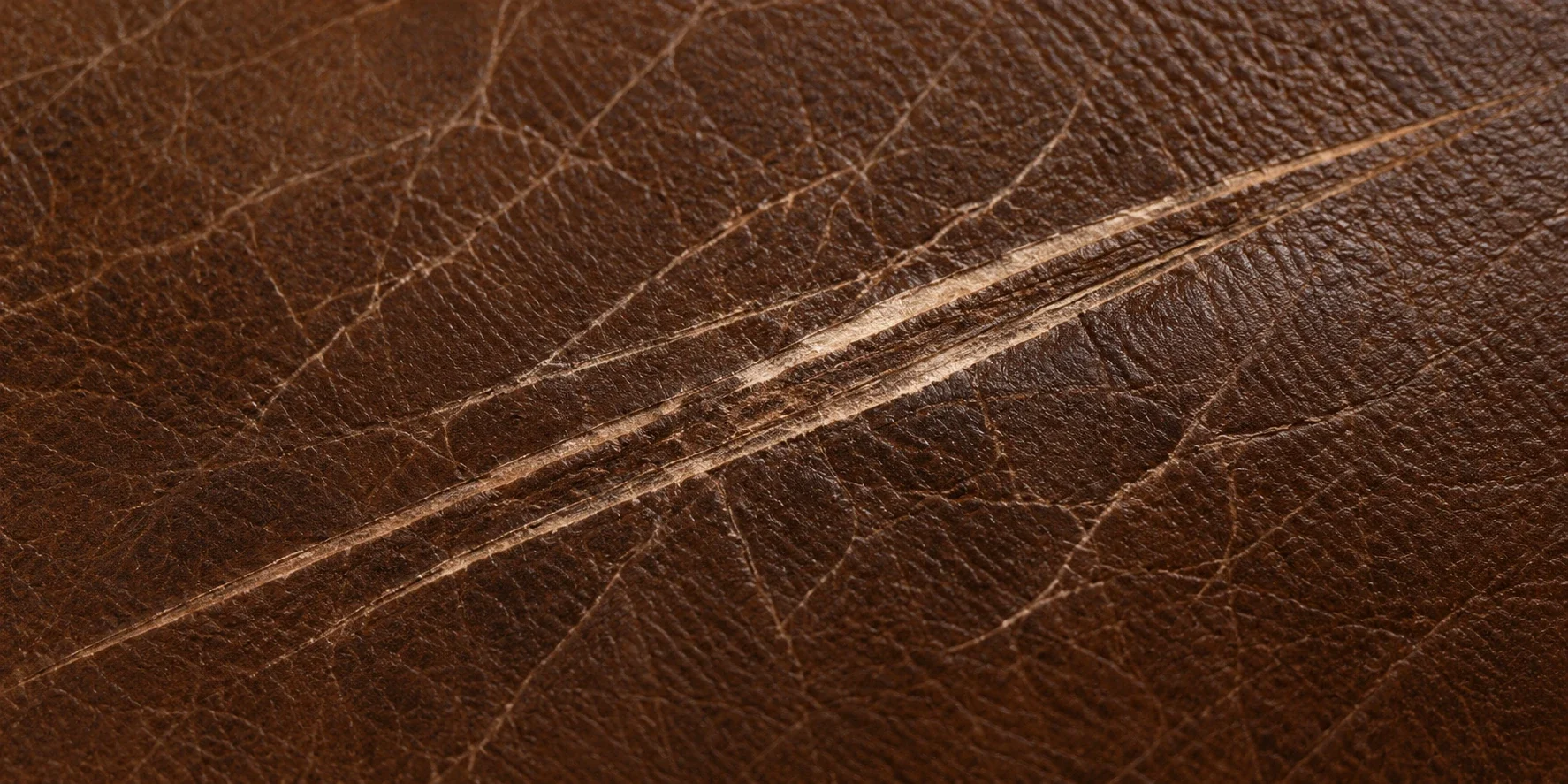 A single pale scratch cut across mid-brown pebbled leather