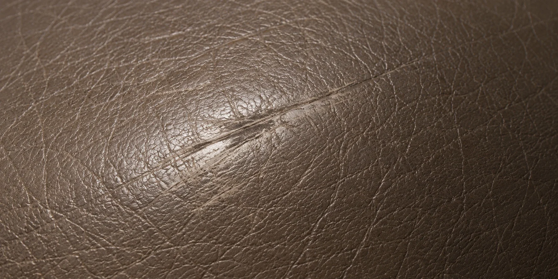 A burnished scuff line raised across a taupe leather cushion edge