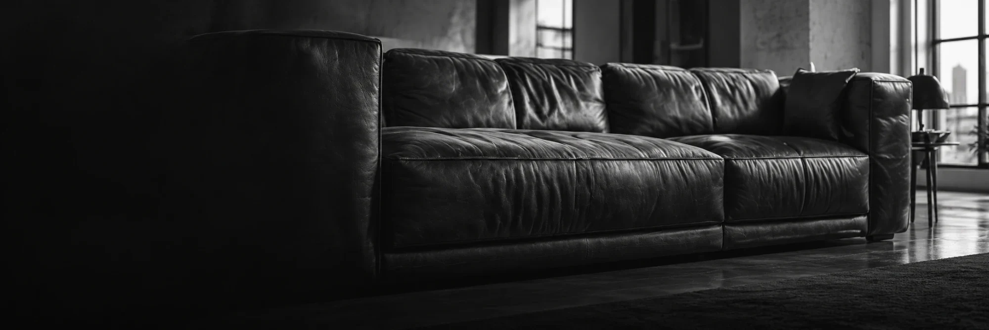 Black and white photograph of a deep leather sofa in a loft with tall windows