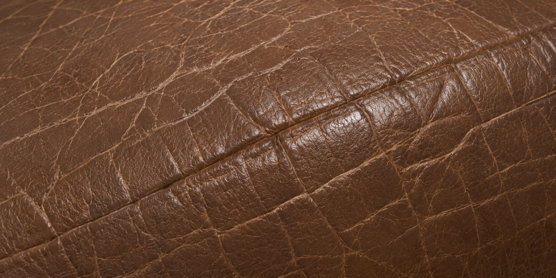 Pale crazing worn along a stitched seam on a brown leather cushion