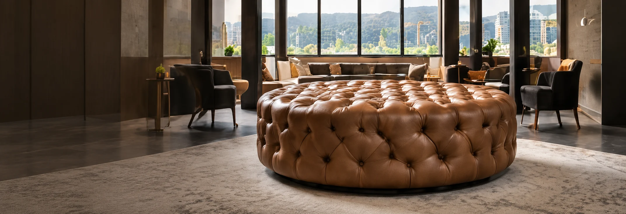 A large round deep-tufted cognac leather ottoman in a hotel lobby with floor-to-ceiling glass
