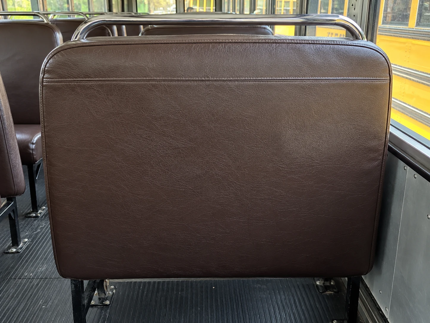 The padded back panel of a school bus seat seen from the row behind
