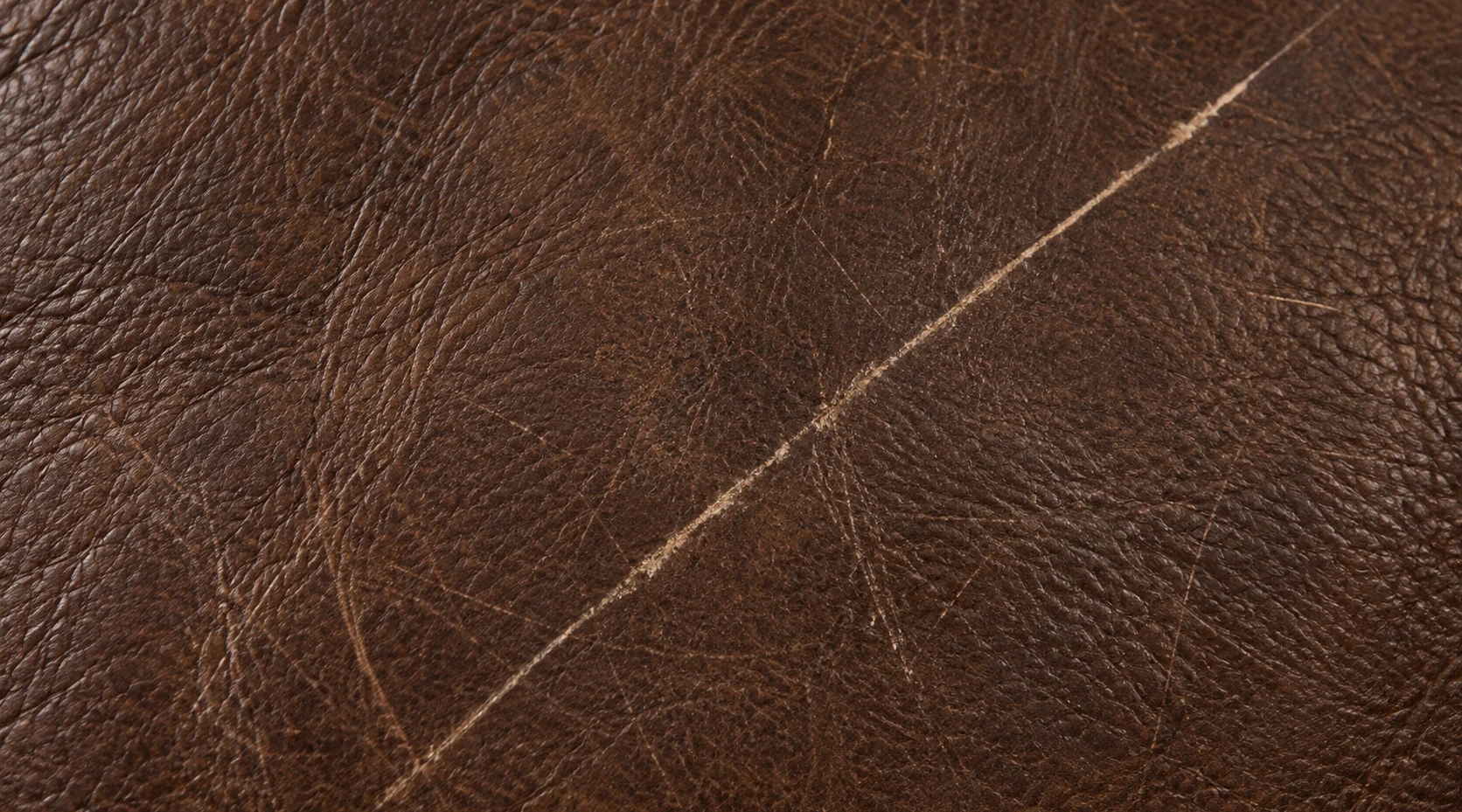One long diagonal scratch across an otherwise sound brown leather bed panel