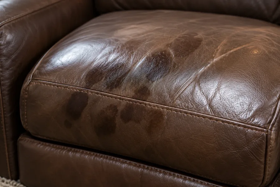 Dark patches of body oil worn into a brown leather seat cushion