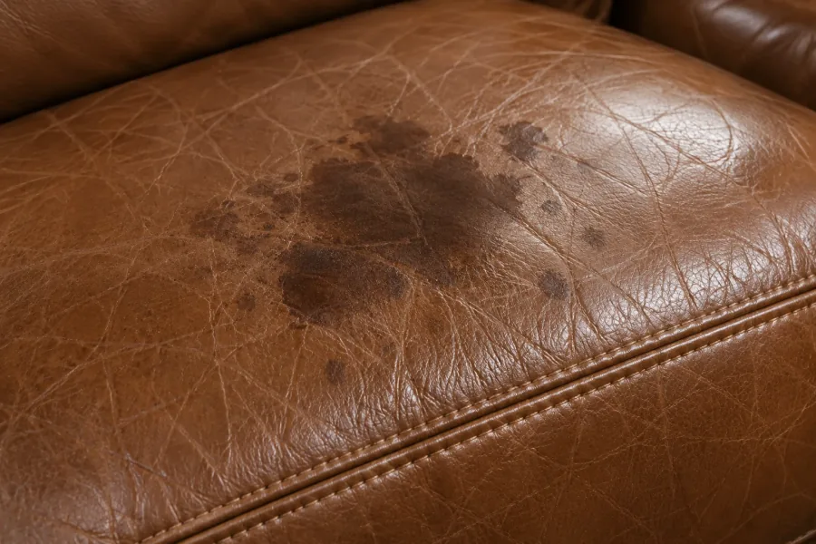 A dark blotchy stain of unknown origin on a tan leather seat cushion