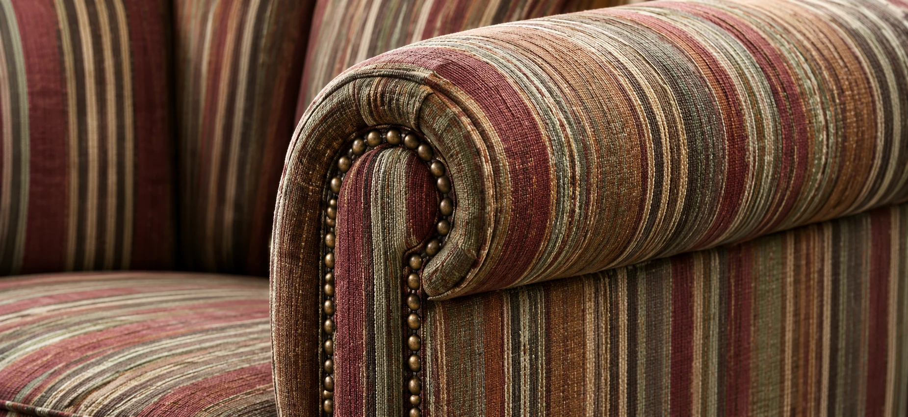 Striped fabric chair arm with brass nailhead trim along the scroll