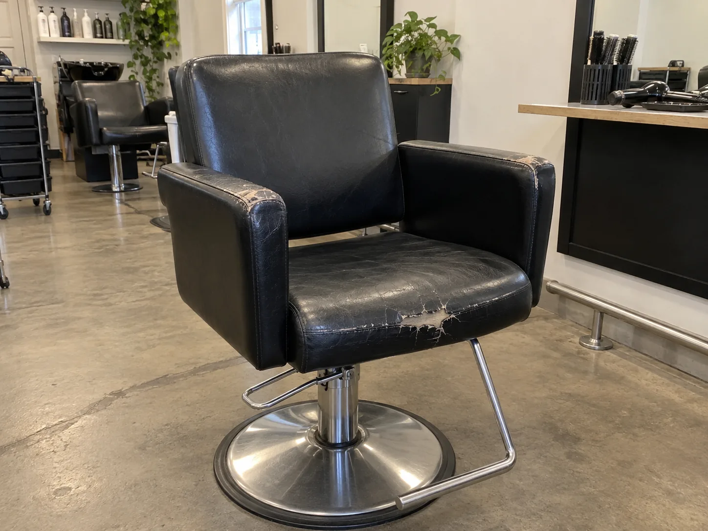 A worn black vinyl styling chair before reupholstery
