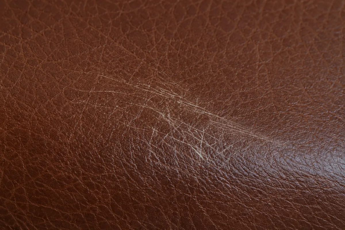 Close-up of a light surface scratch on brown leather, damage sitting in the topcoat only