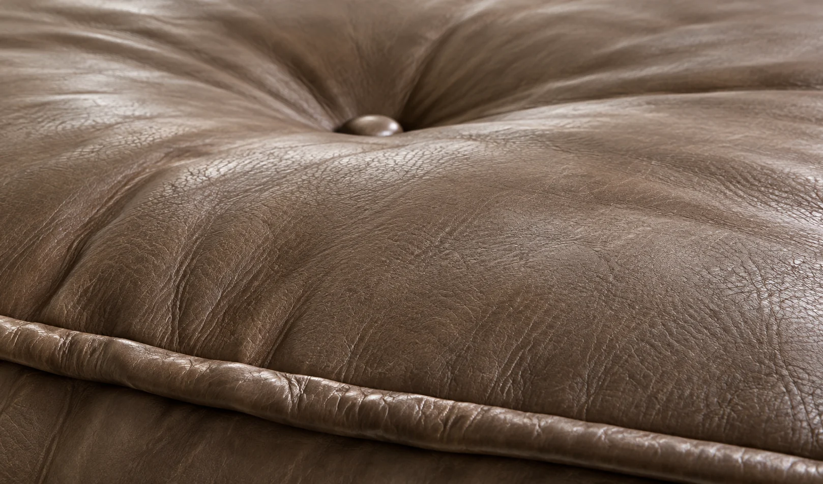 A single button pulled deep into a taupe leather surface, the fold gathering around it