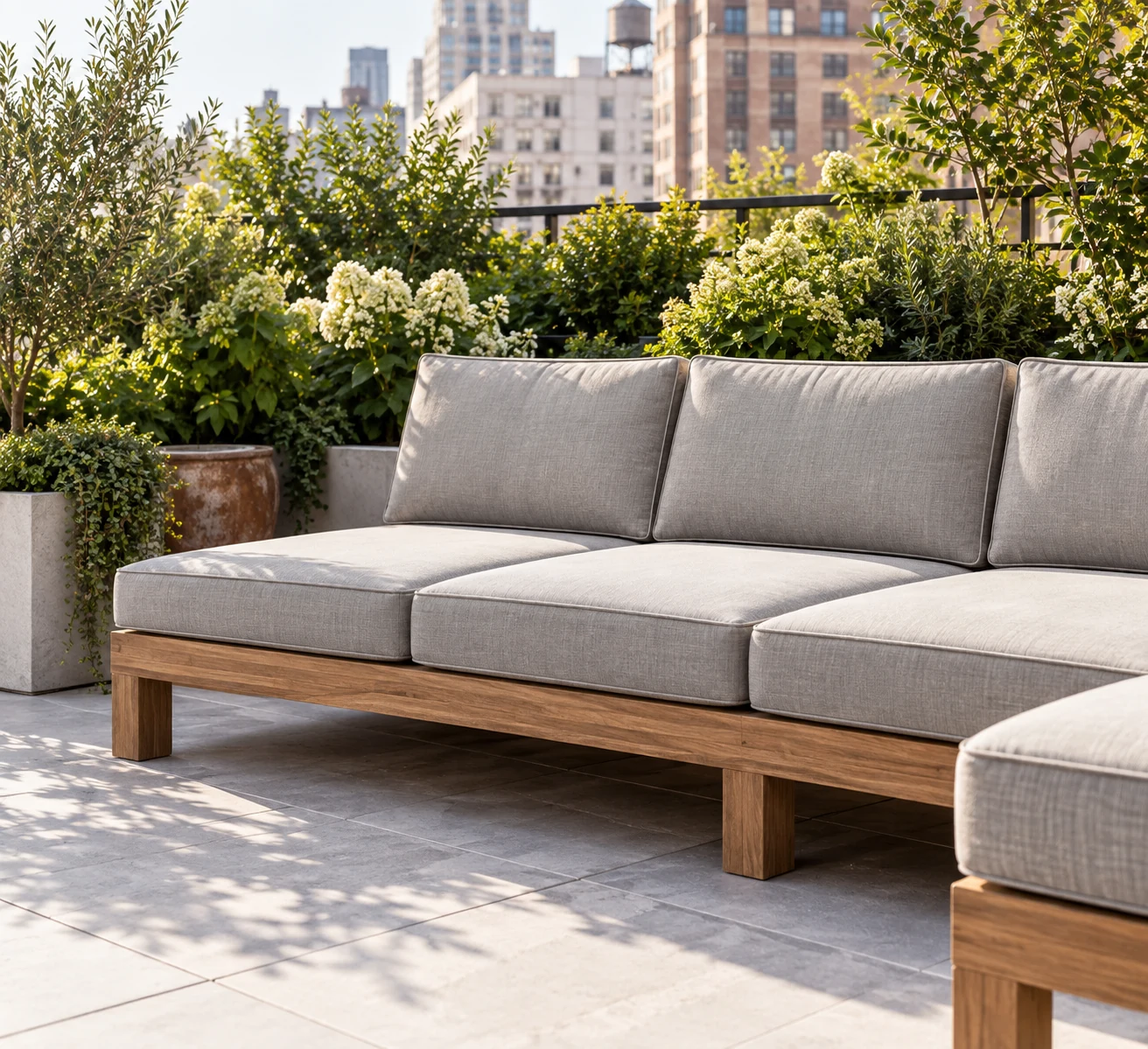 Teak outdoor sectional with grey box cushions on a planted city terrace