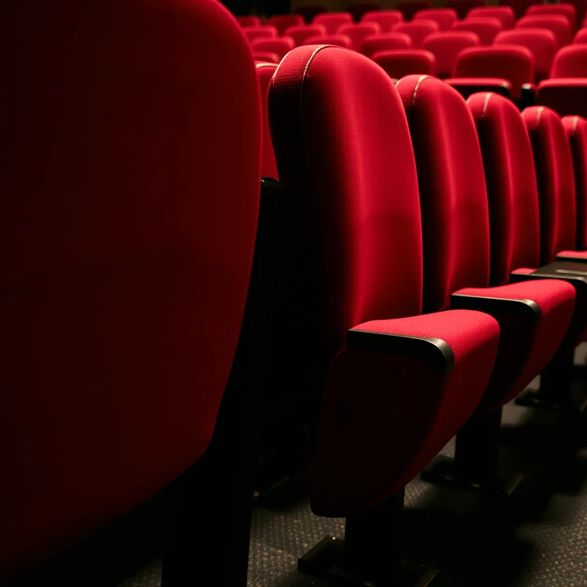 An empty row of deep red upholstered theatre seats with dark armrest caps, seen at an angle from the aisle end