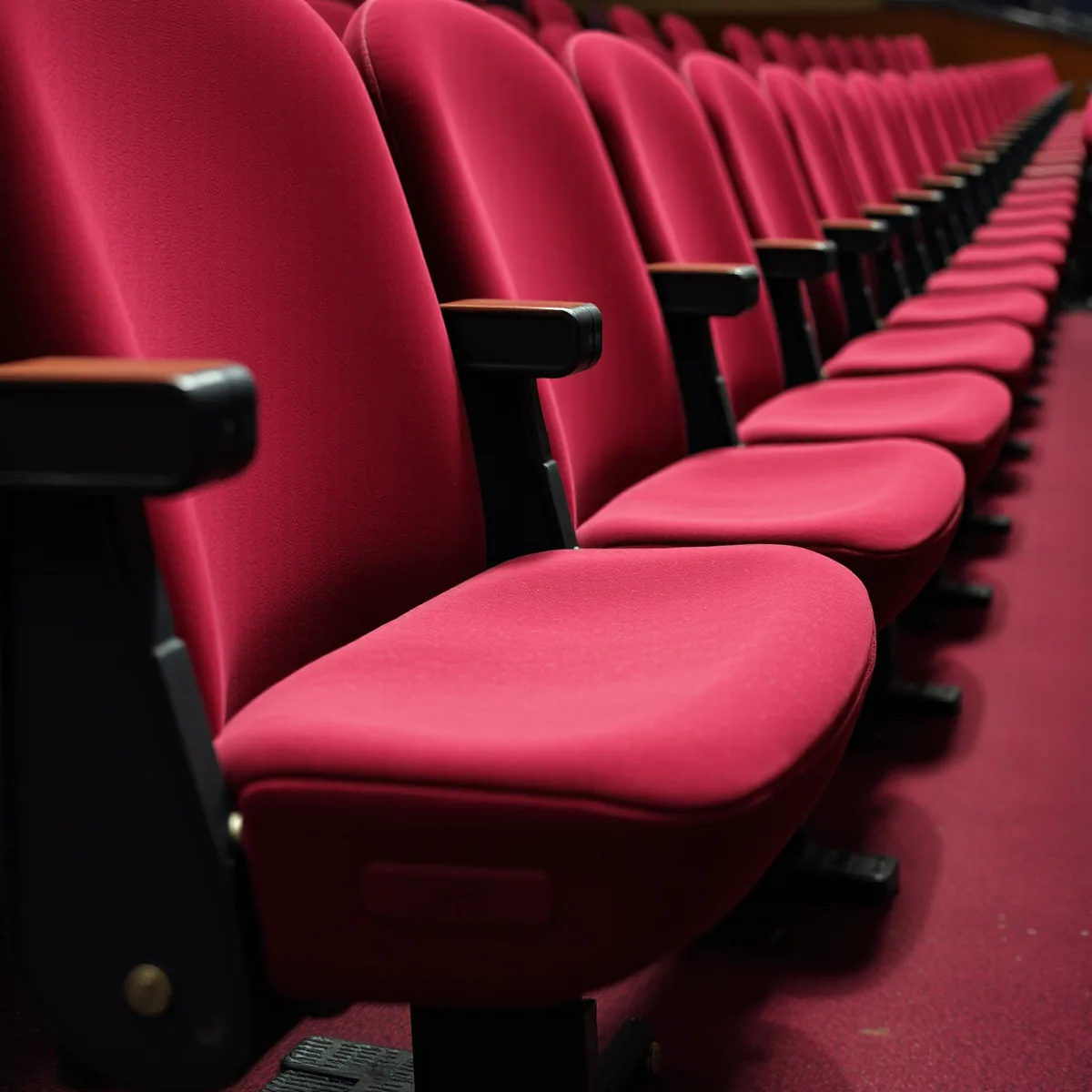 A receding row of freshly recovered deep red upholstered theatre seats with dark armrests, seen from the side along the row