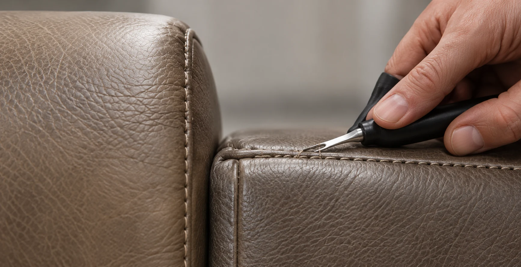 A hand using a small tool along a seam on a taupe leather bed panel
