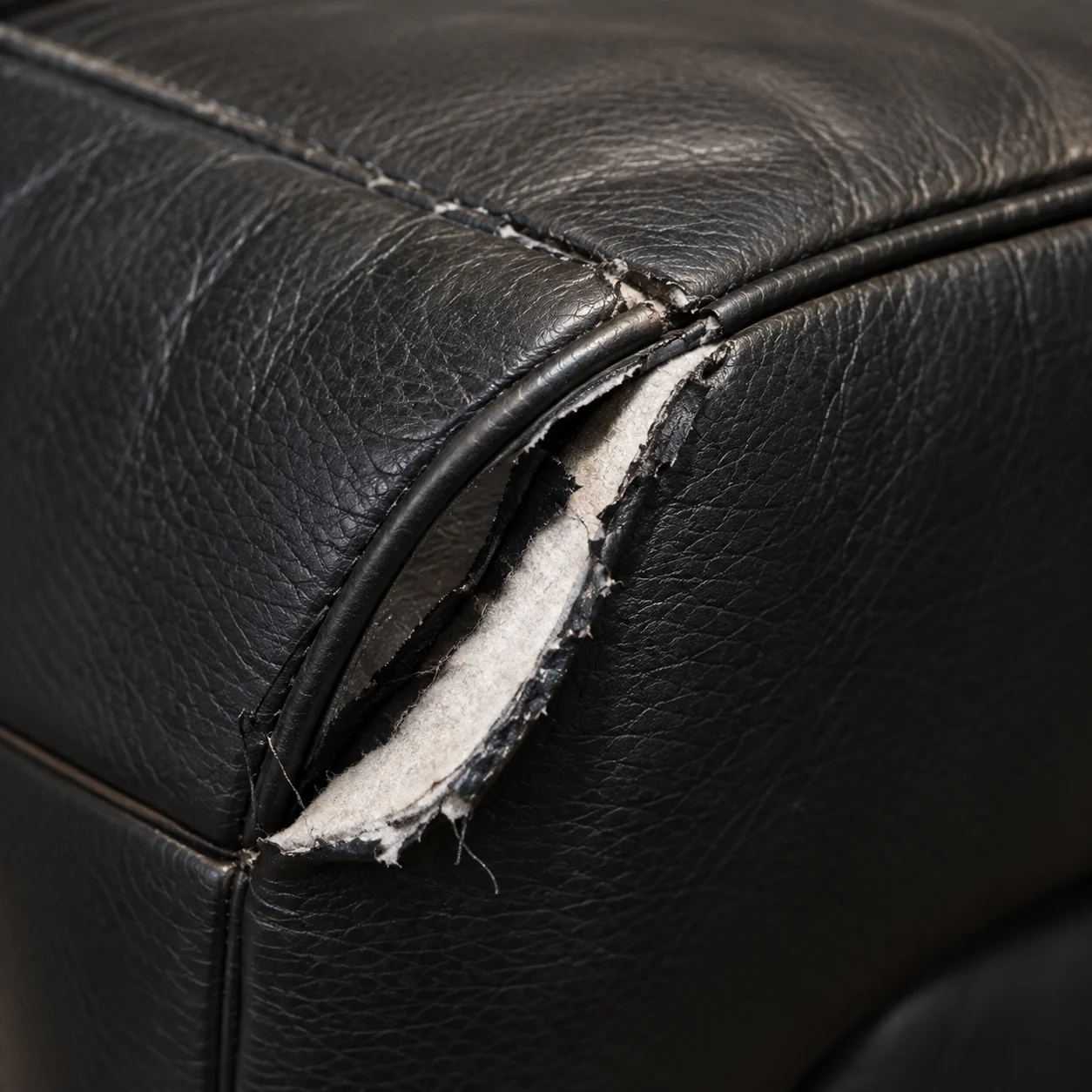 A torn corner of black leather on a massage chair with white batting showing through