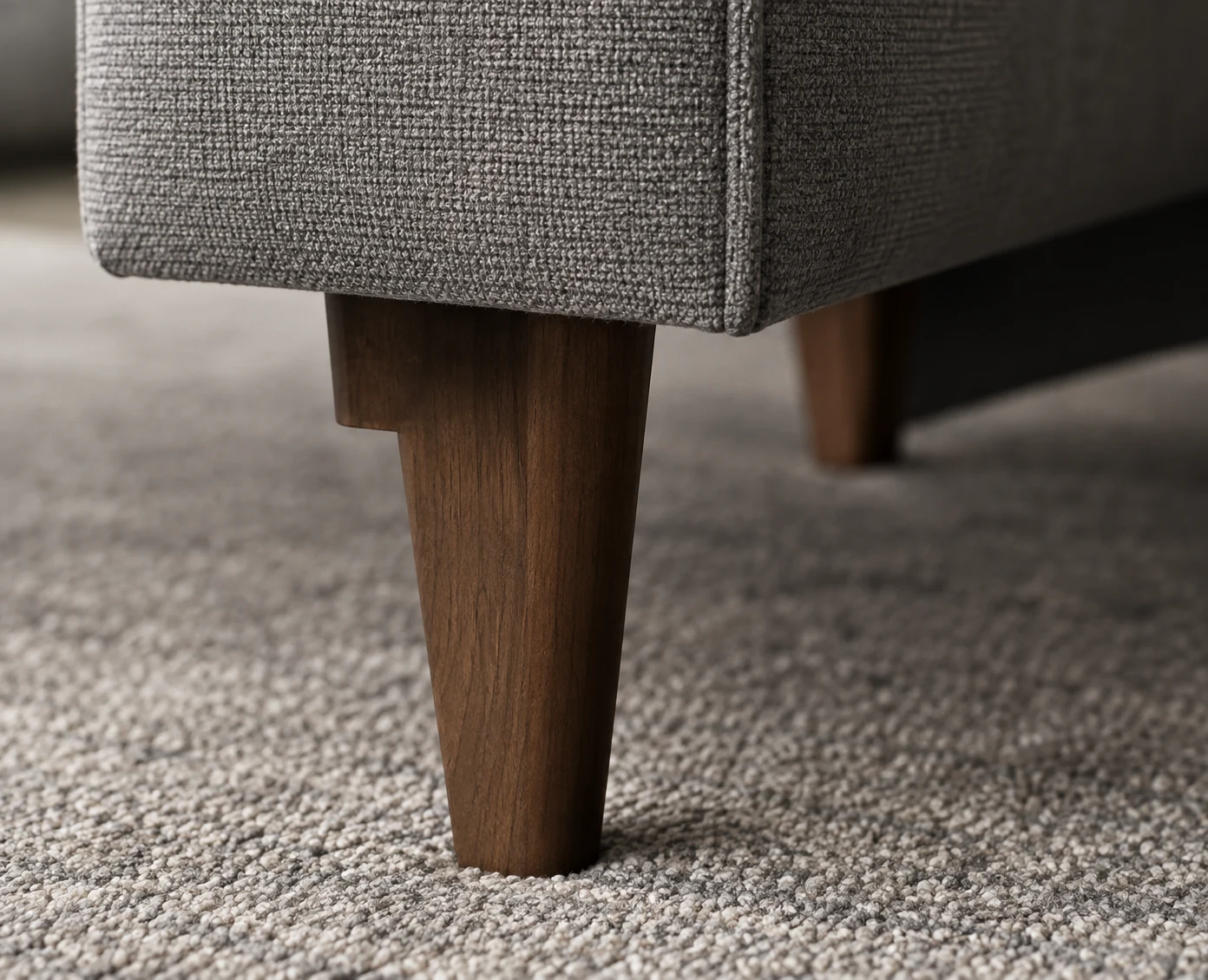 Tapered walnut leg under an upholstered sofa corner