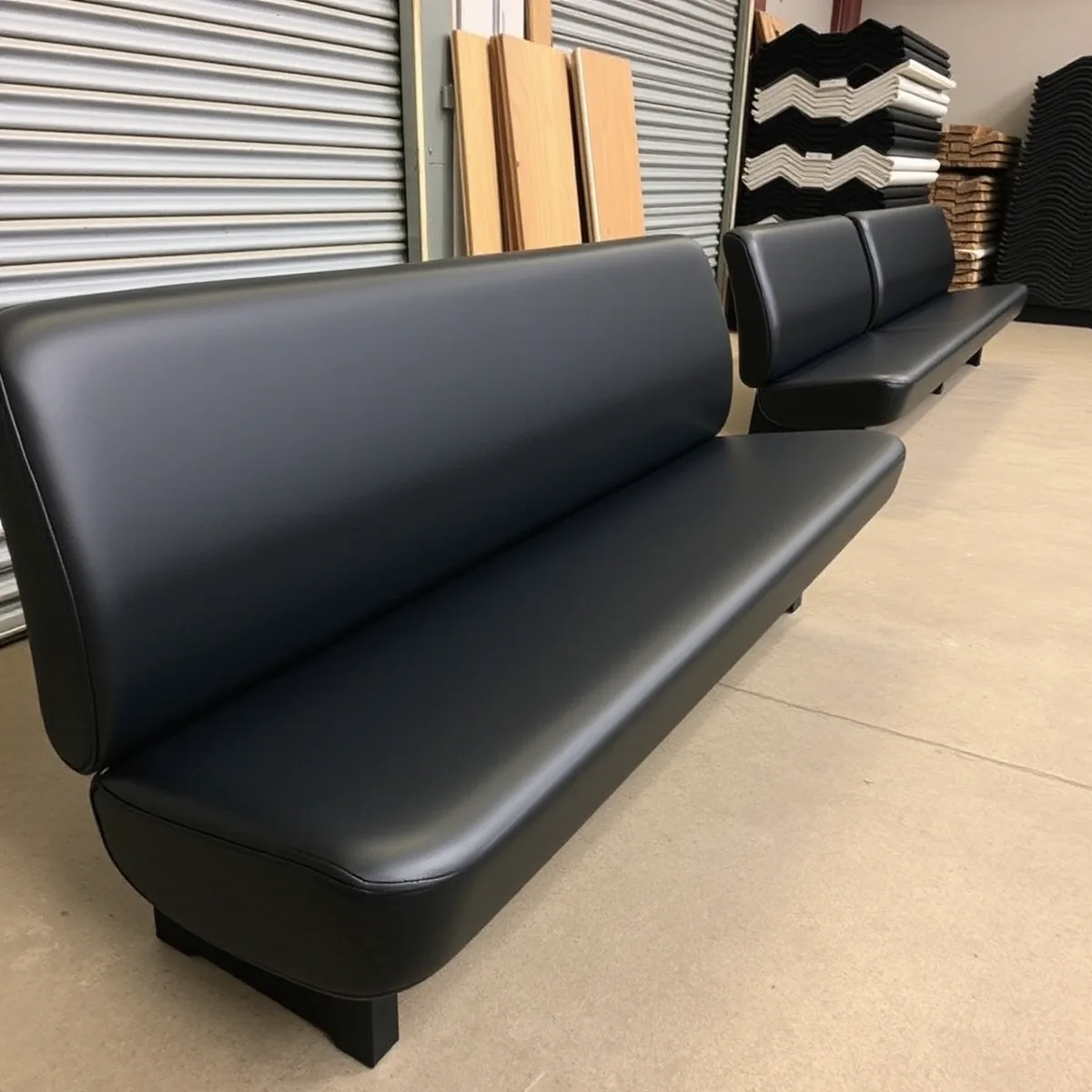 Row of refinished dark vinyl bench seats standing on a shop floor waiting to be refitted