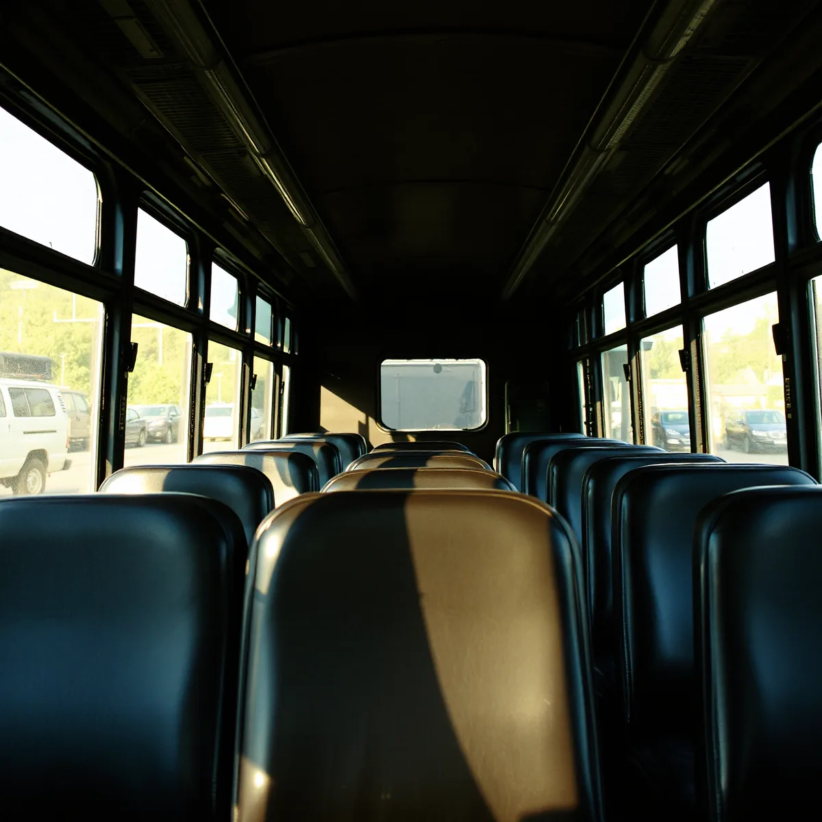 Afternoon sunlight falling in bands across a row of dark vinyl bench seats inside a parked bus