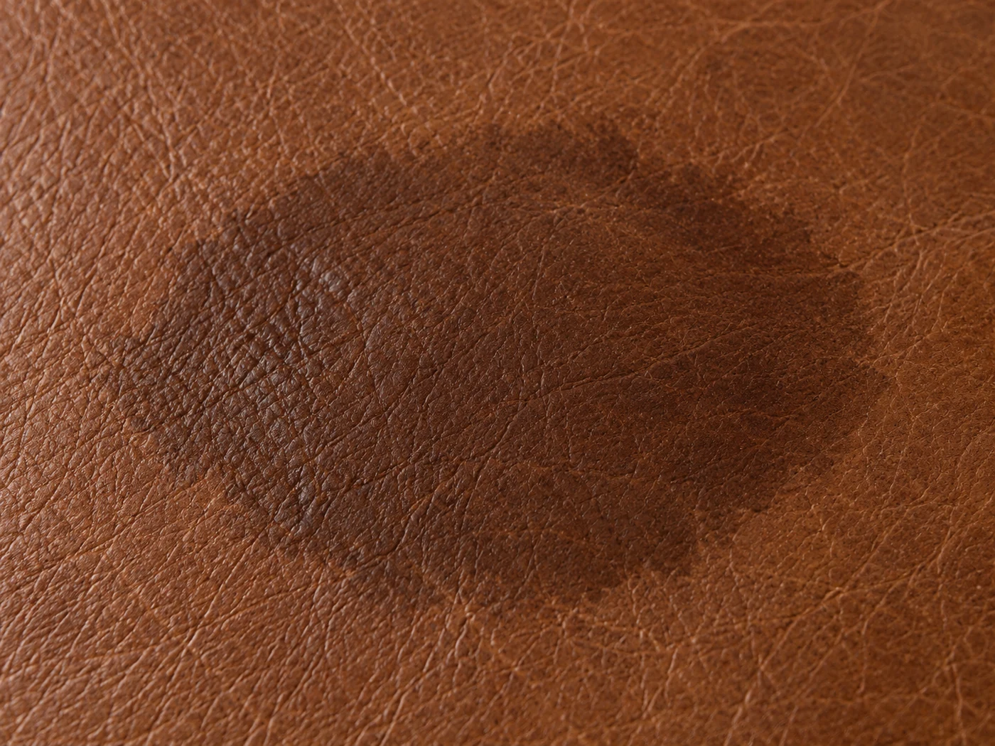 Water absorbed into brown aniline leather, leaving a dark saturated patch with a soft edge