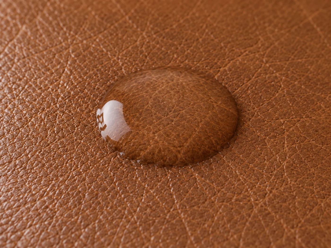 A drop of water on brown semi-aniline leather, still beaded but starting to wet the grain at its rim
