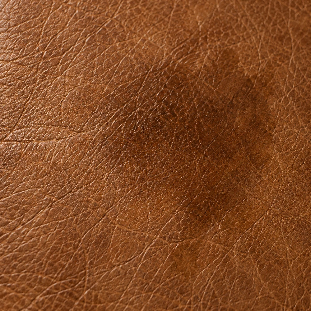 Brown leather with a soft diffuse dark patch where water has wicked outward through the fibre