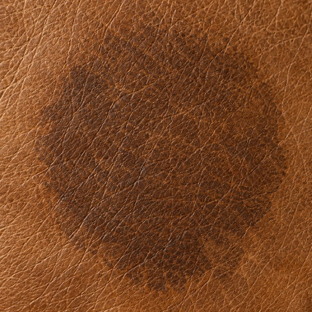 Brown leather with a dense saturated dark disc where the wet patch has loaded with salts and dye